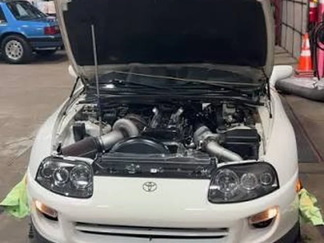White Toyota Supra with a large single turbo, bonnet open in a workshop